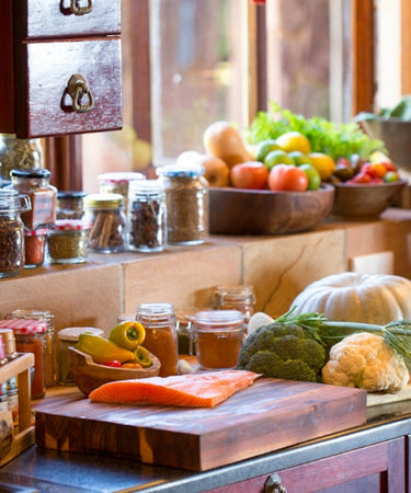 Fresh ingredients on kitchen countertop including salmon, vegetables, and spices in jars.