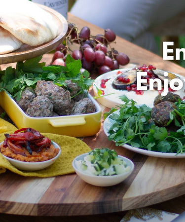 A beautiful outdoor dining setup with assorted grilled dishes, fresh herbs, and pita bread, promoting enjoyment of the sun.