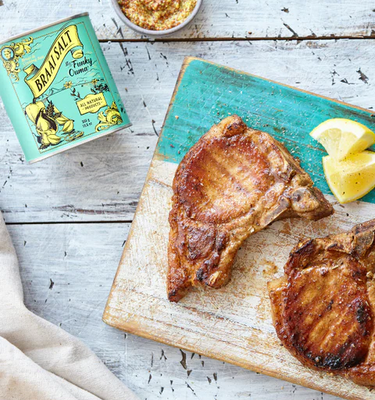 Grilled pork chops on a chopping block with Funky Ouma Braai Salt and lemon slices.