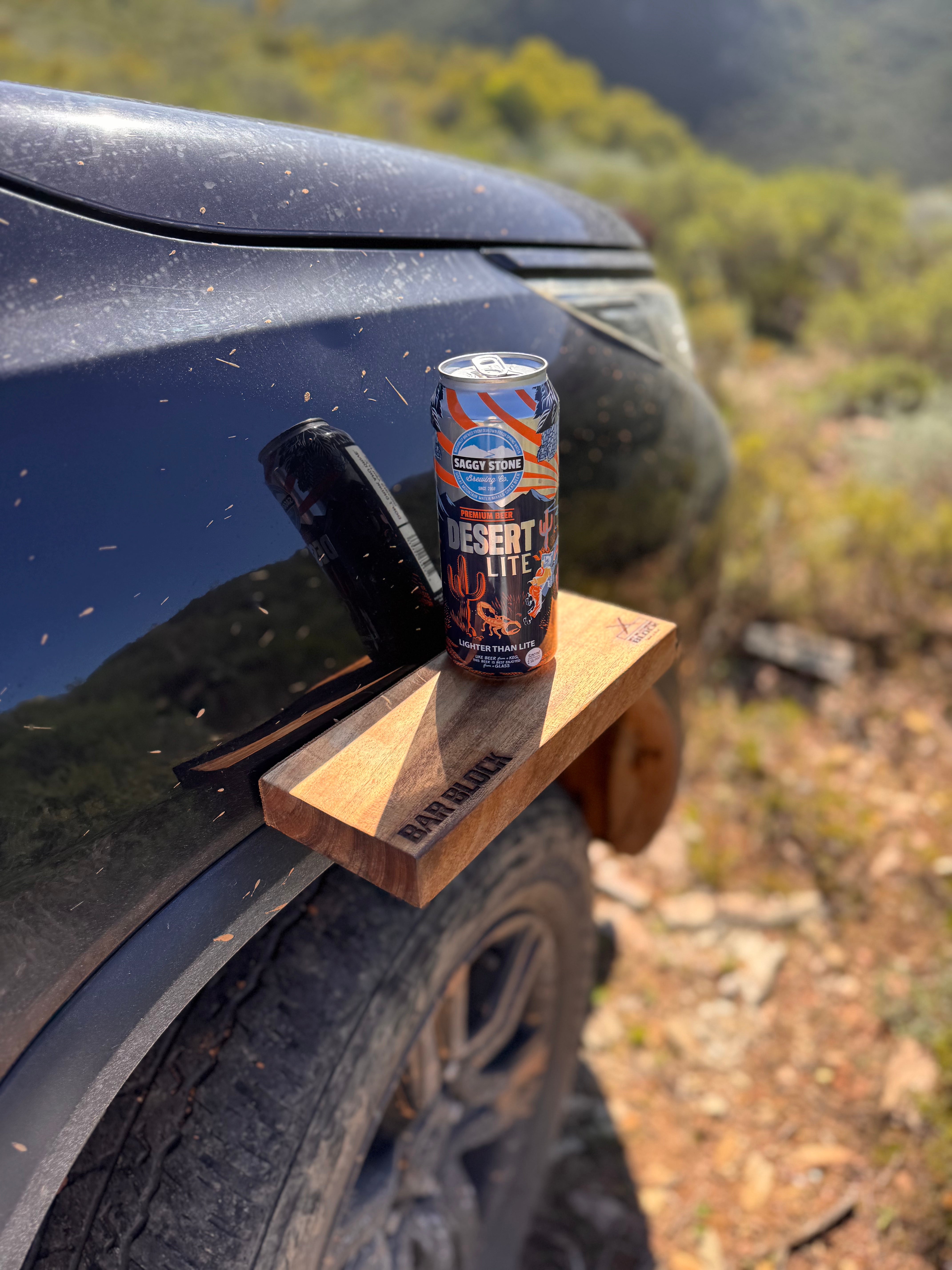 Can of 'Desert Storm' energy drink on a wooden block attached to a car in a natural setting