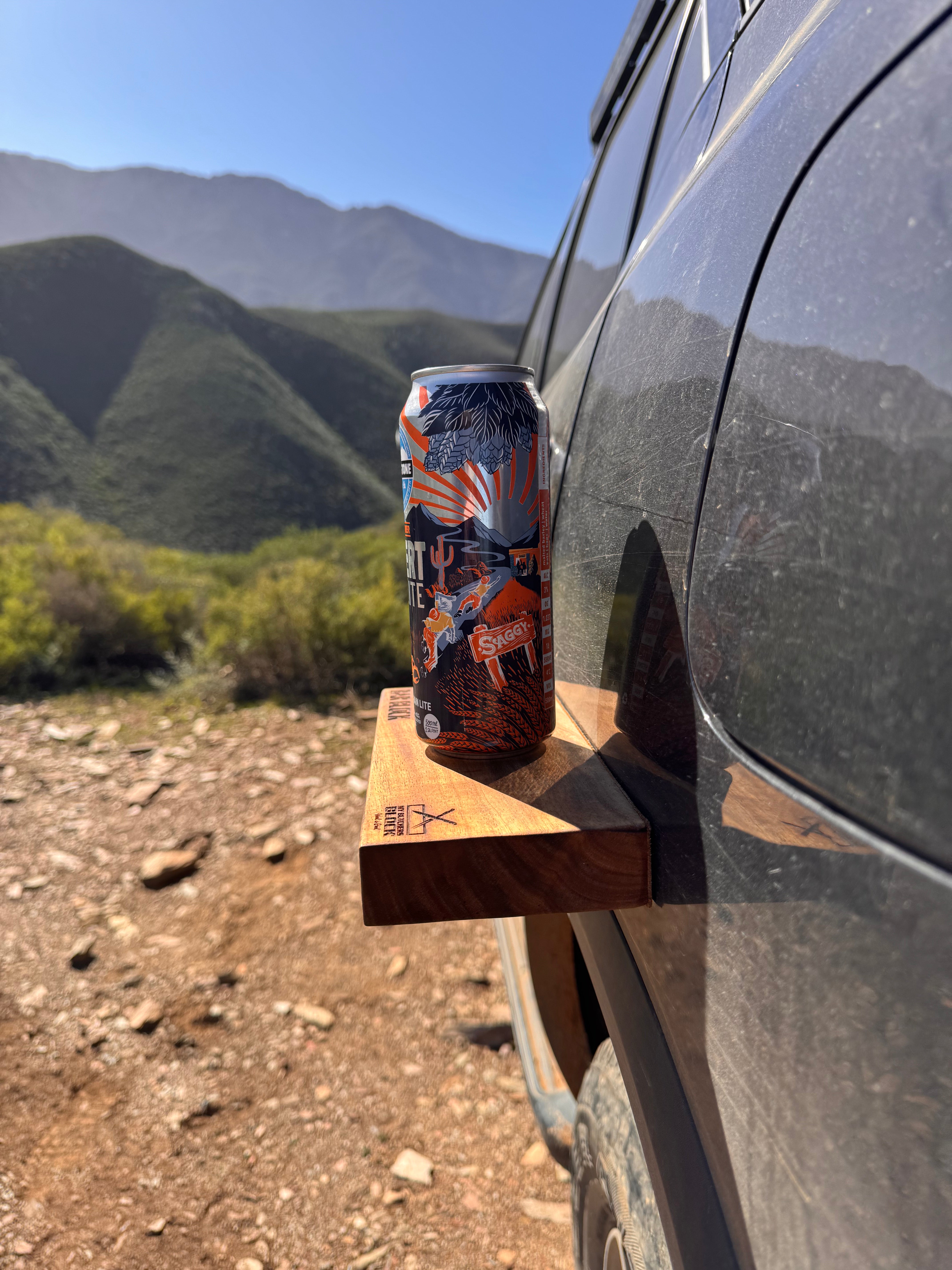 Can of Monster Energy Drink attached to a car window with mountains in the background