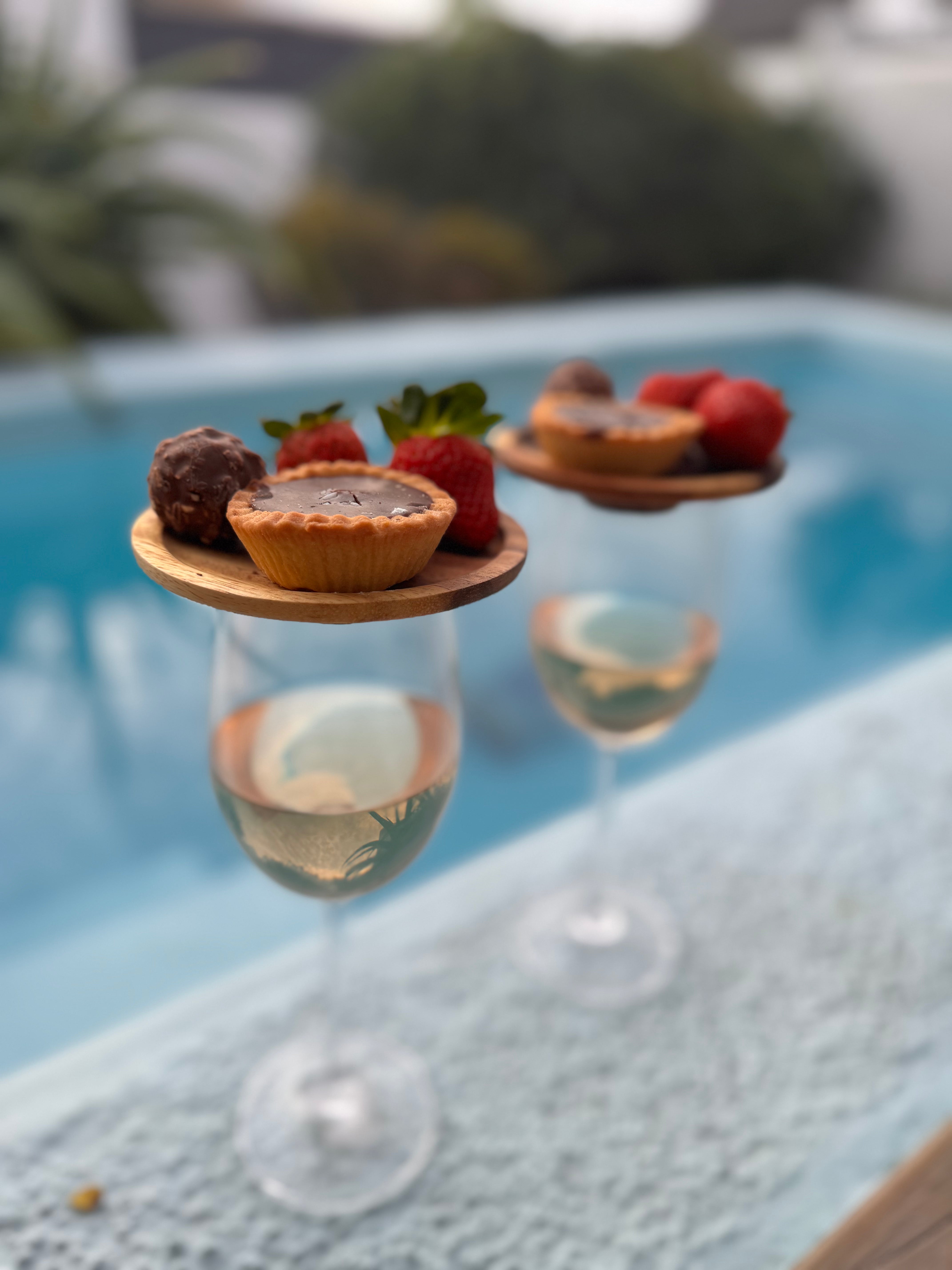 Desserts on small wooden platforms over a glass of champagne by a pool.