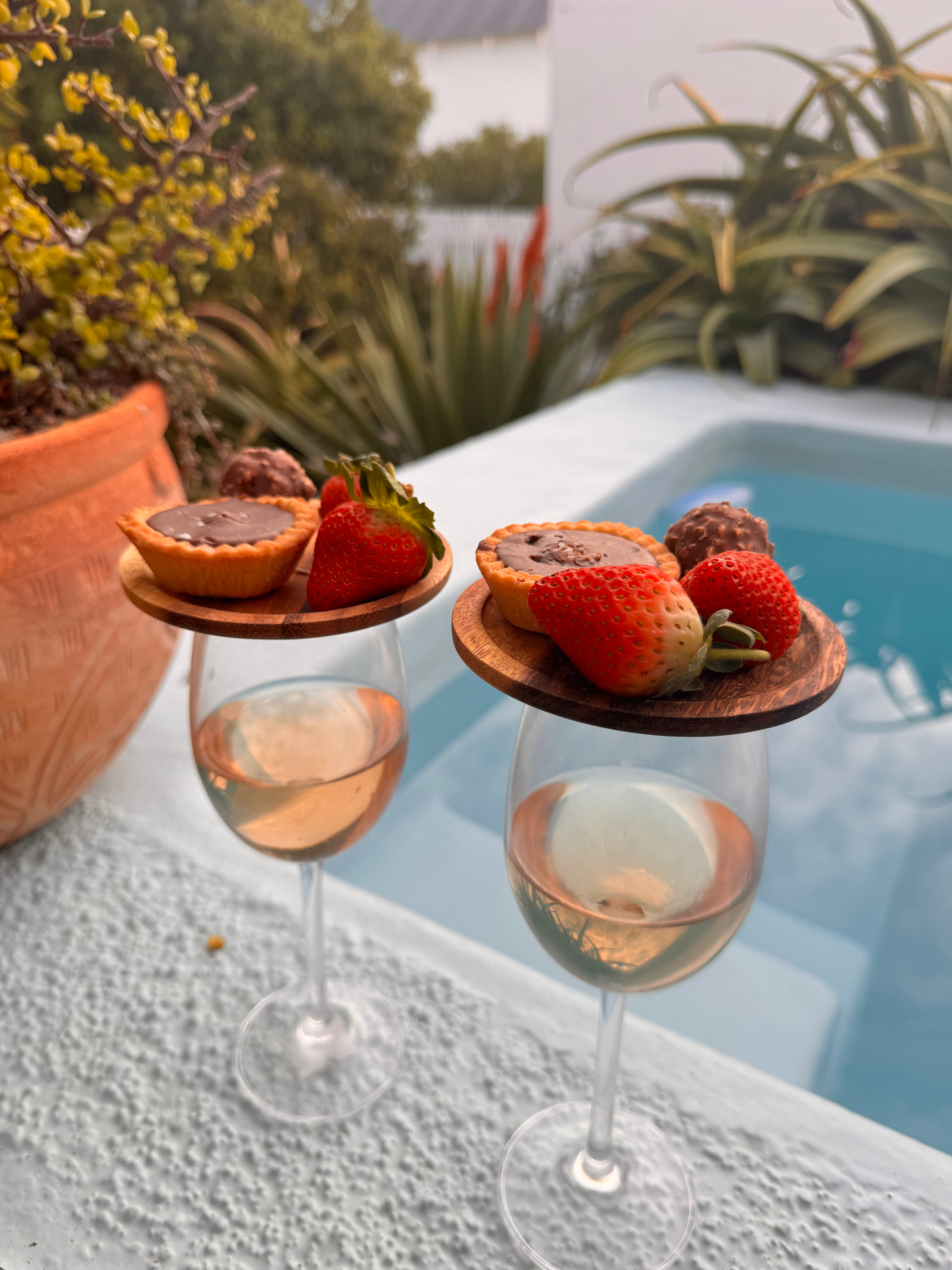 Two wine glasses with fruit and dessert garnishes by a poolside.