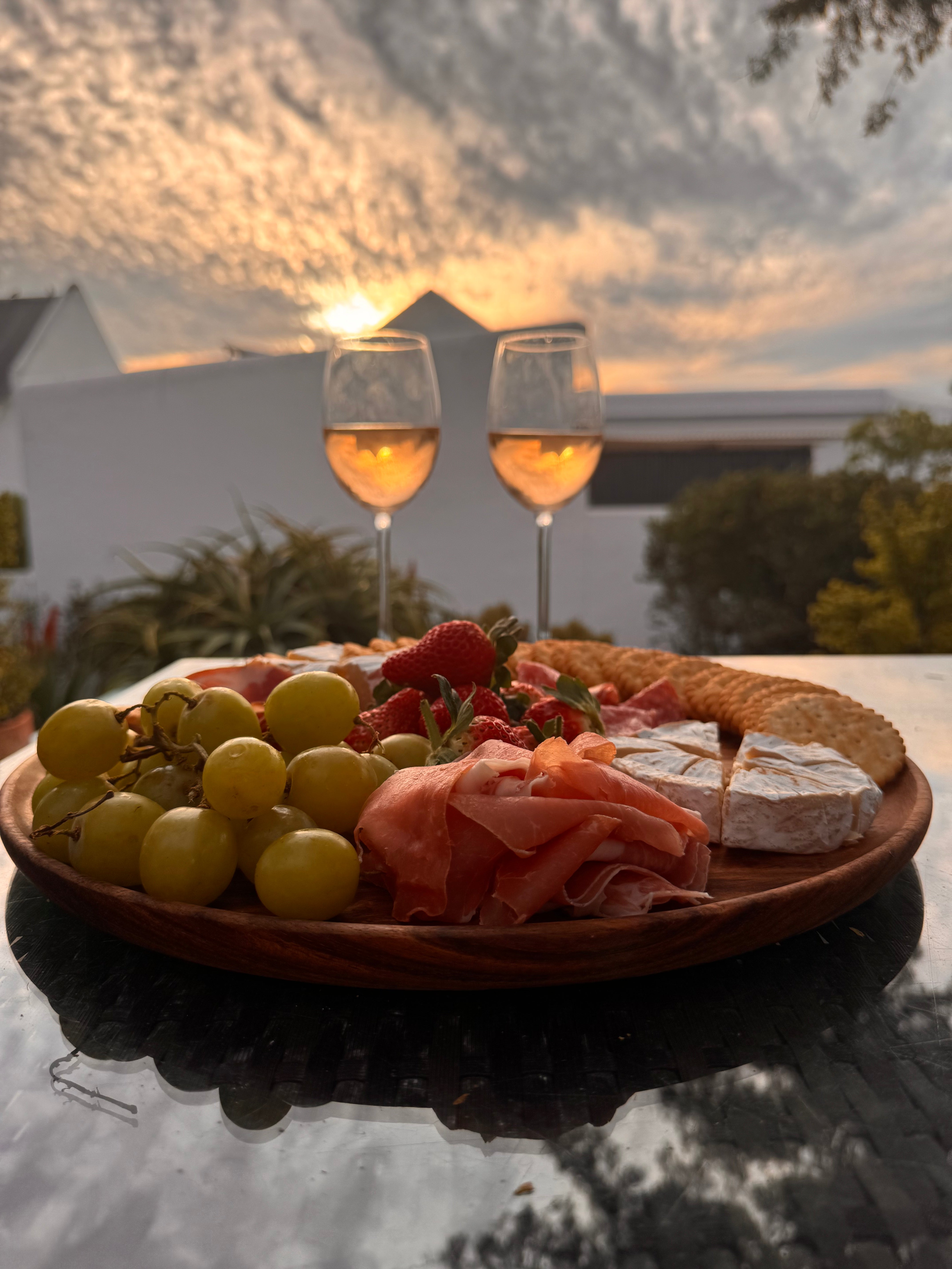 Platter of food with wine glasses on a table outdoors during sunset.