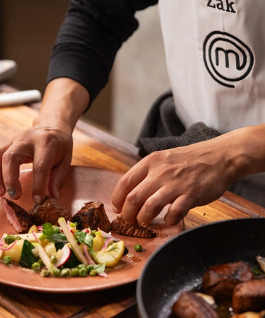 Chef plating gourmet dish with meat and vegetables, showcasing culinary skills in the kitchen.